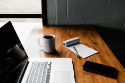 Image of desk with open laptop, coffee mug, notepad and pen, and iPhone