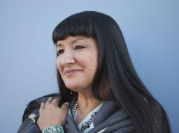Sandra Cisneros looks off to the left standing against a blue background